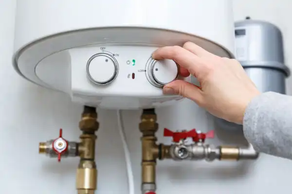 A hand adjusts the temperature settings on a white water heater tank, showcasing the intricate valves and pipes below, a crucial step in efficient boiler installation.