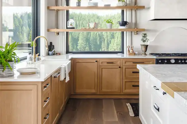 Modern kitchen with wooden cabinets, white countertops, and a large window showcasing lush greenery. Floating shelves with plants and kitchenware. Bright and airy space with natural light, maintained in perfect condition thanks to recent plumbing repair ensuring everything flows smoothly.