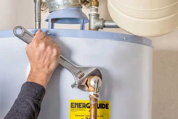 A person engages in water heater repair, using a wrench to tighten a pipe joint while the "EnergyGuide" label remains prominently visible.