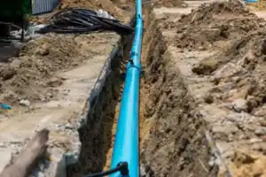 Home Service Blogs | Levine &Amp; Sons Plumbing, Heating, &Amp; Cooling A Blue Pipe, Part Of The Water Line Installation, Is Laid In A Narrow Trench Surrounded By Dirt And Construction Materials.