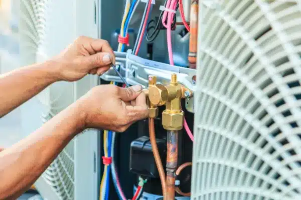 Hands of a technician meticulously performing air conditioning maintenance, adjusting wires and components amidst a vibrant array of colorful cables and metal parts.
